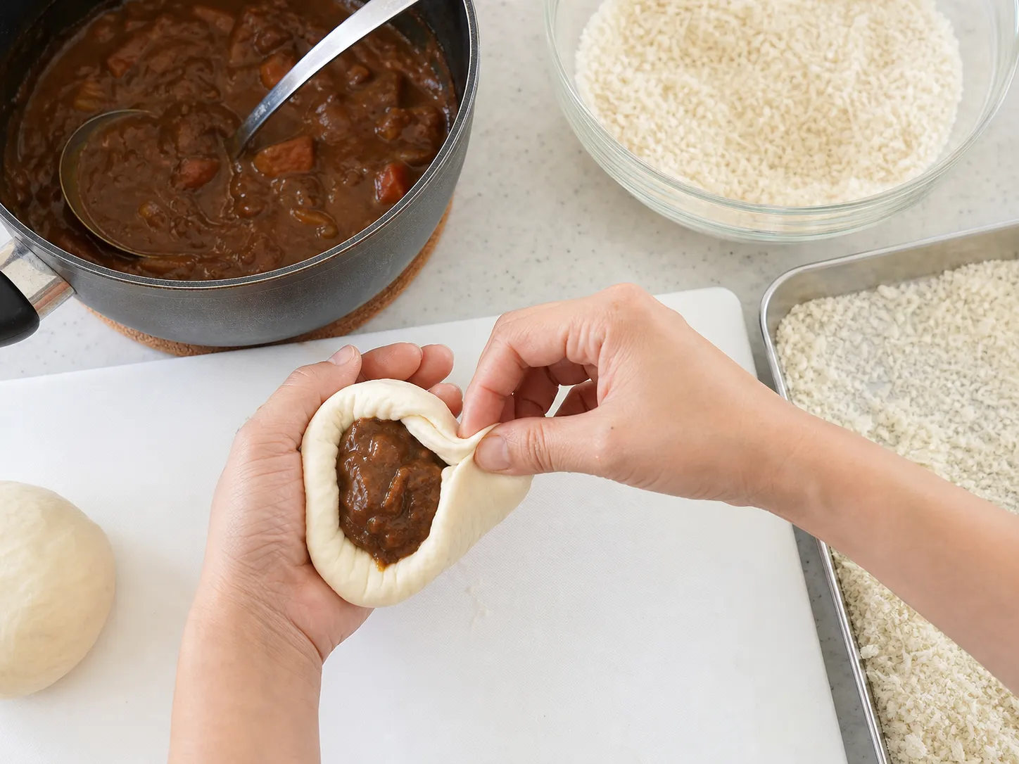 Hands wrapping Japanese curry in bread dough and rolling it in panko breadcrumbs before deep frying