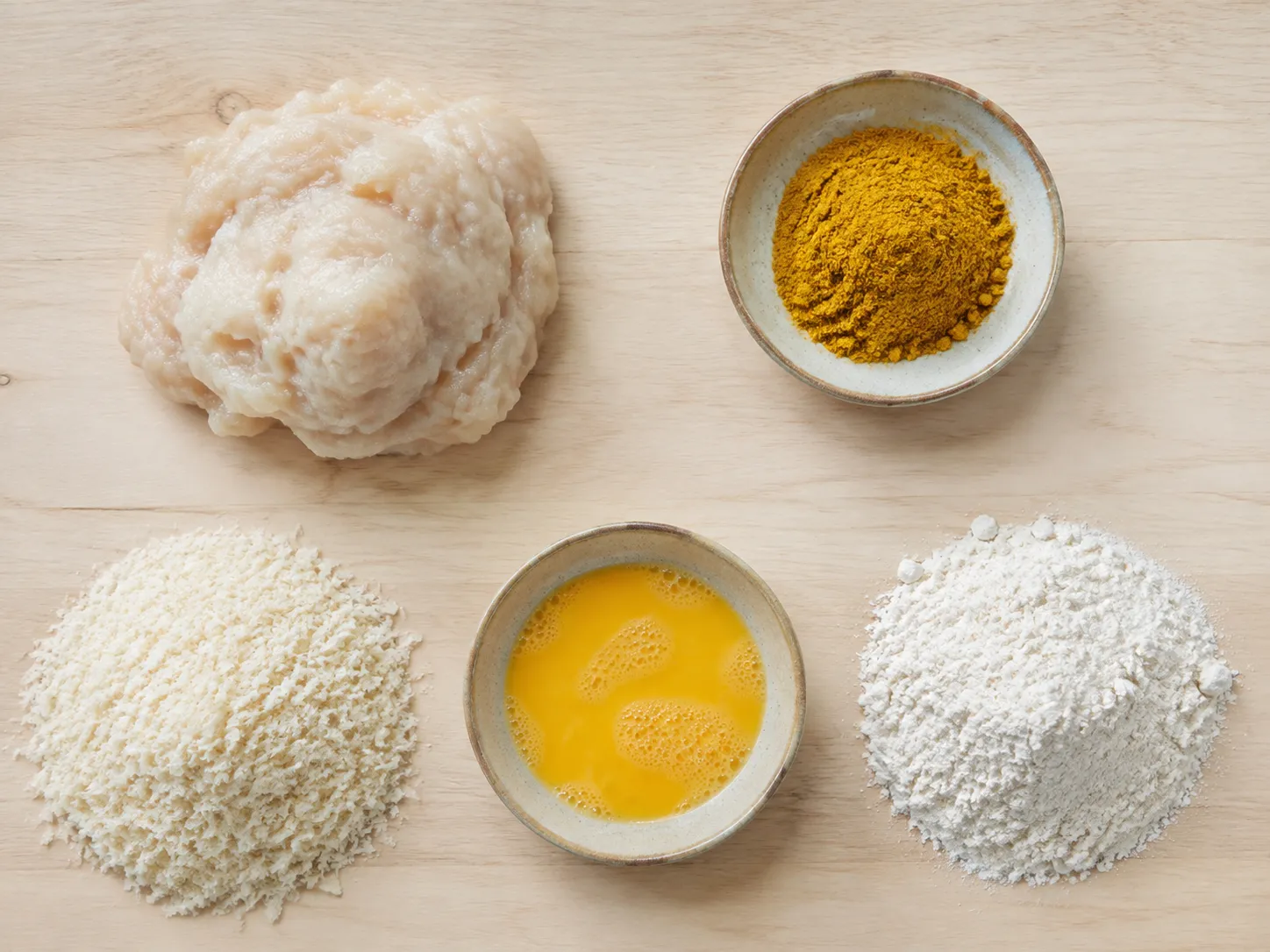 Flat lay of fish katsu ingredients: raw white fish paste, curry powder, panko, beaten egg and flour