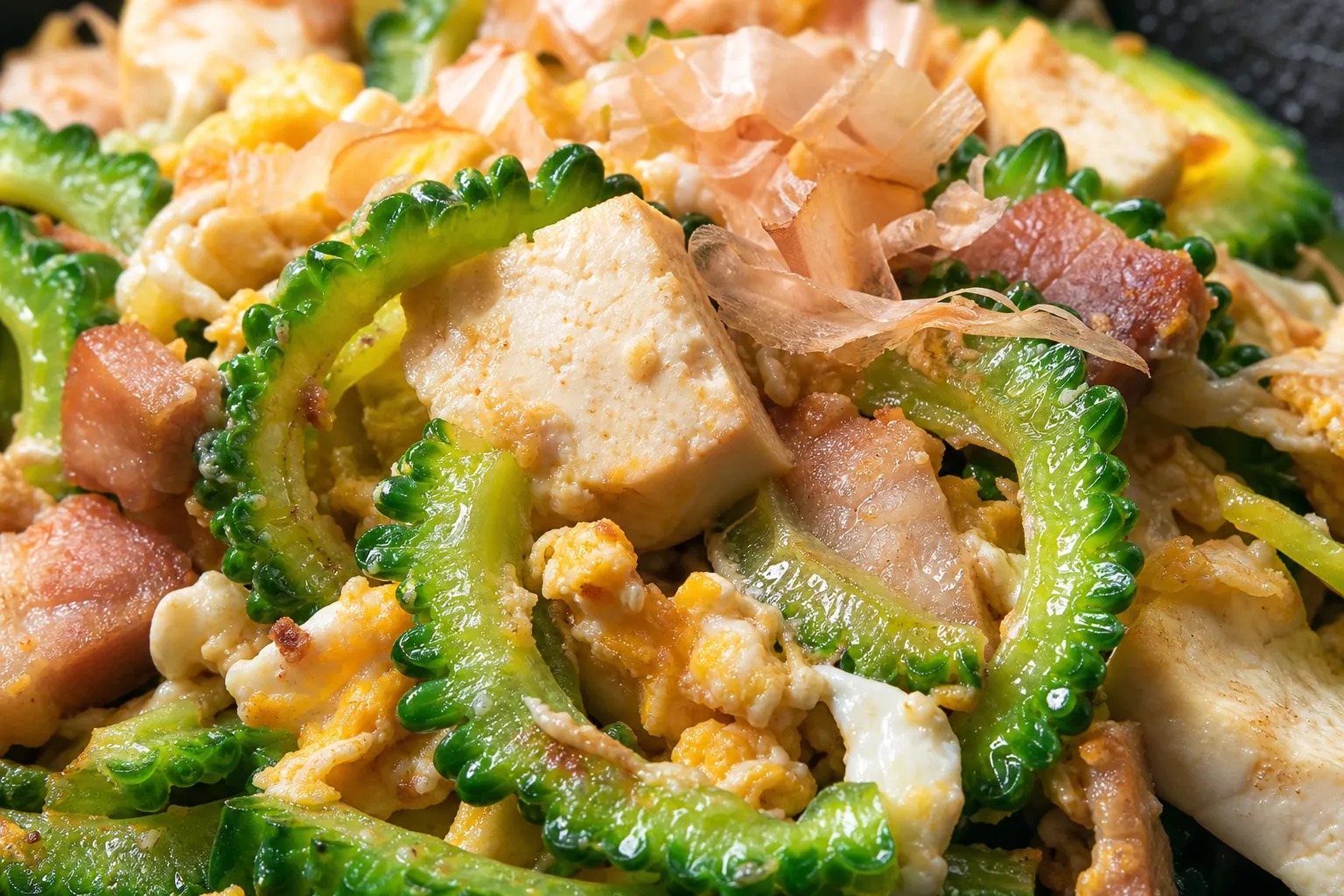 Close-up of goya chanpuru showing green bitter melon slices, tofu, egg and pork with bonito flakes