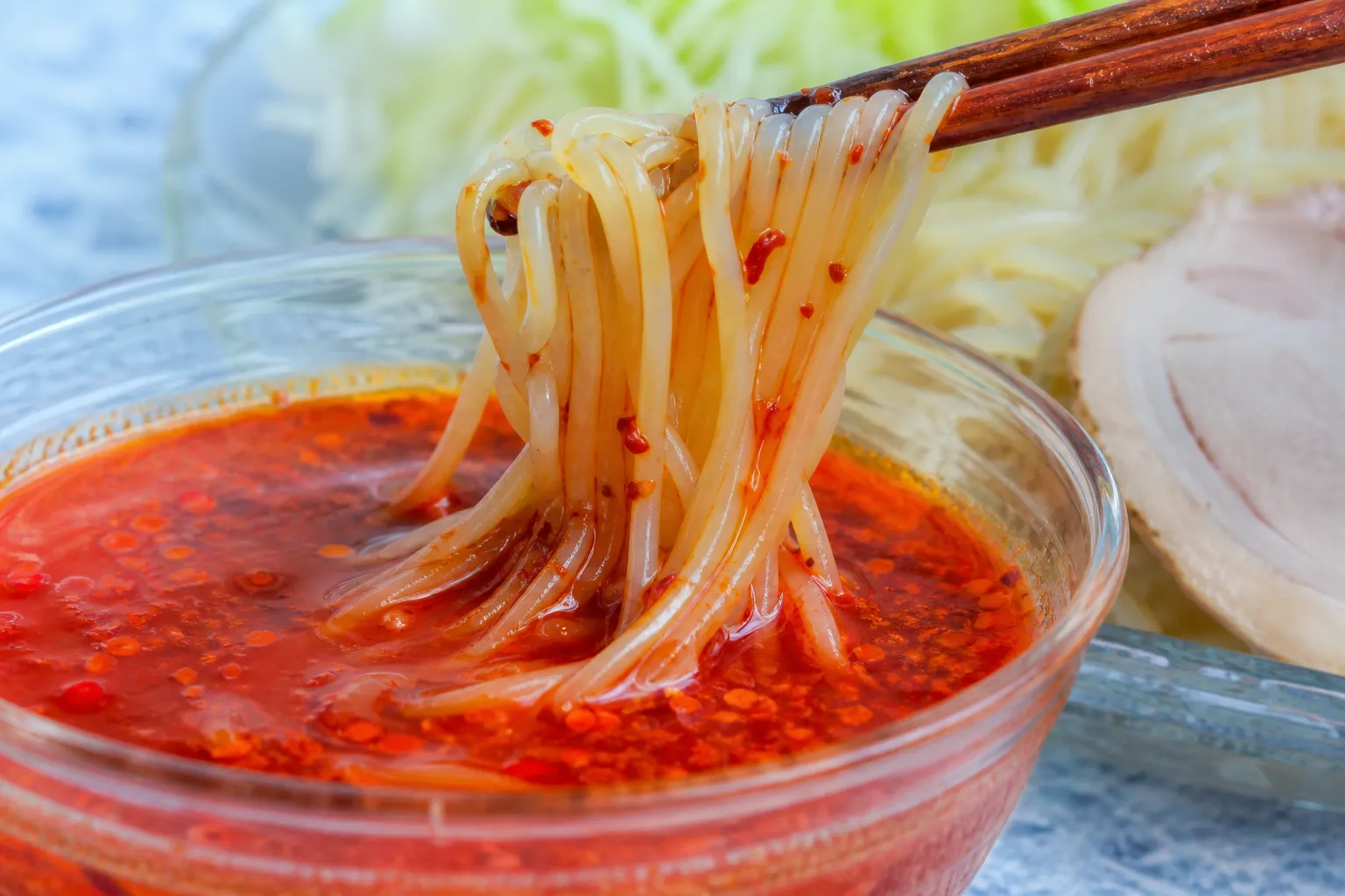 Close-up of chilled noodles being dipped into red spicy sauce