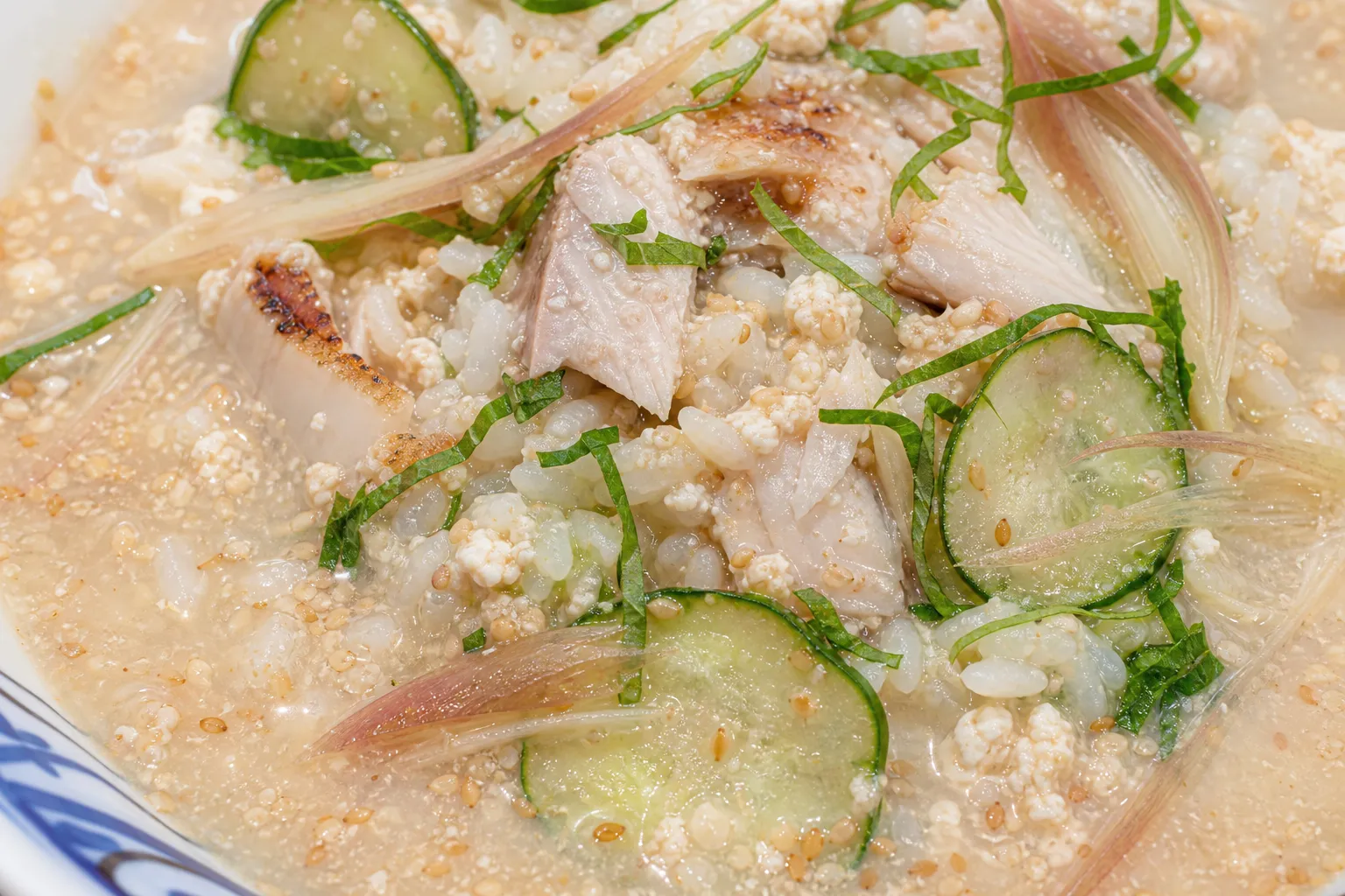Close-up of cold sesame-miso hiyajiru broth with cucumber, shiso and tofu over rice