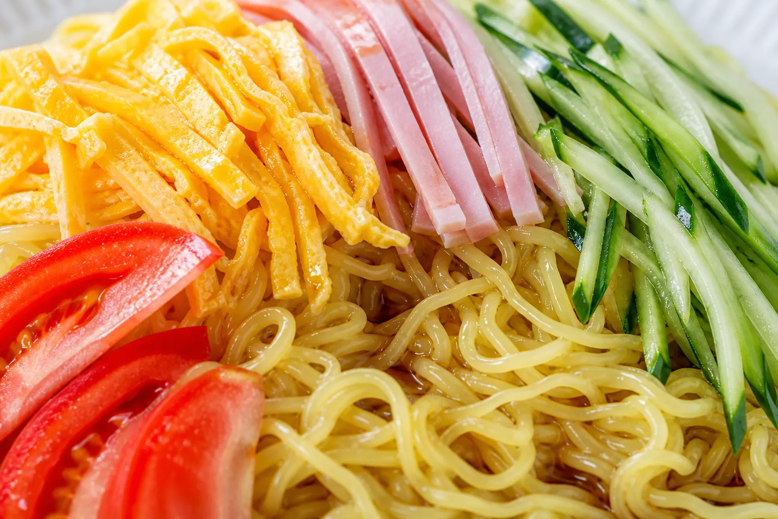 Close-up of chilled hiyashi chuka noodles with colorful strips of egg, ham, cucumber and tomato in tangy sauce