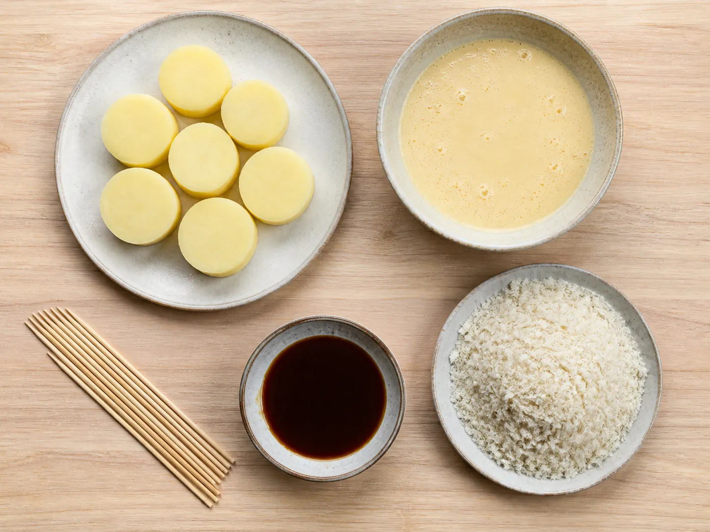 Flat lay of imo-furai ingredients: boiled potato rounds, bamboo skewers, panko, batter, and dark sauce