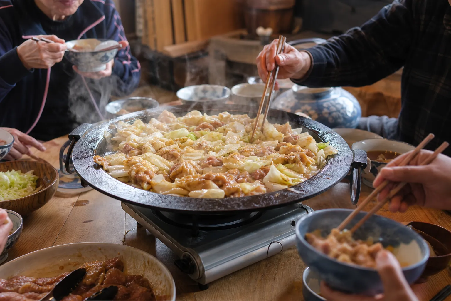 A big iron pan of keichan shared over a tabletop burner at a rustic gathering