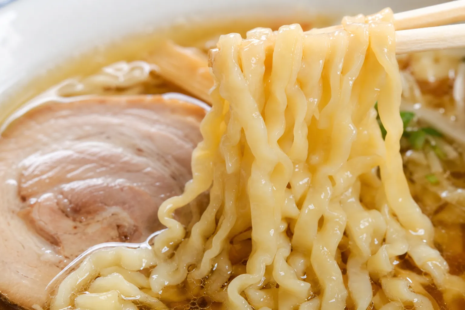 Close-up of the flat, wide, curly noodles of Kitakata ramen in clear broth