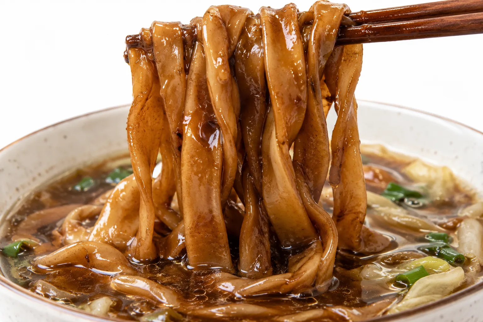 Close-up of flat thick chewy yakisoba noodles being lifted from the clear broth, sauce still clinging to them
