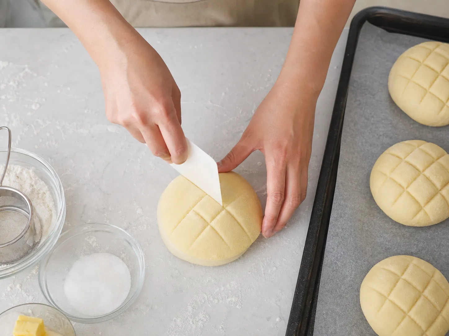 Baker scoring a crosshatch pattern into cookie dough draped over bread dough to make melonpan