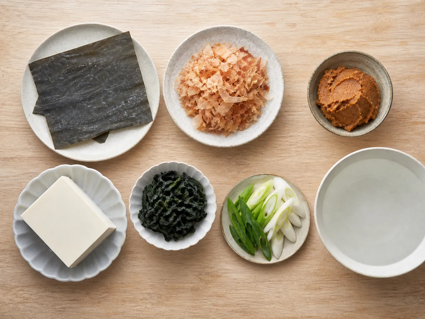 A top-down arrangement of kombu, bonito flakes, miso, tofu, wakame and negi used to make miso soup