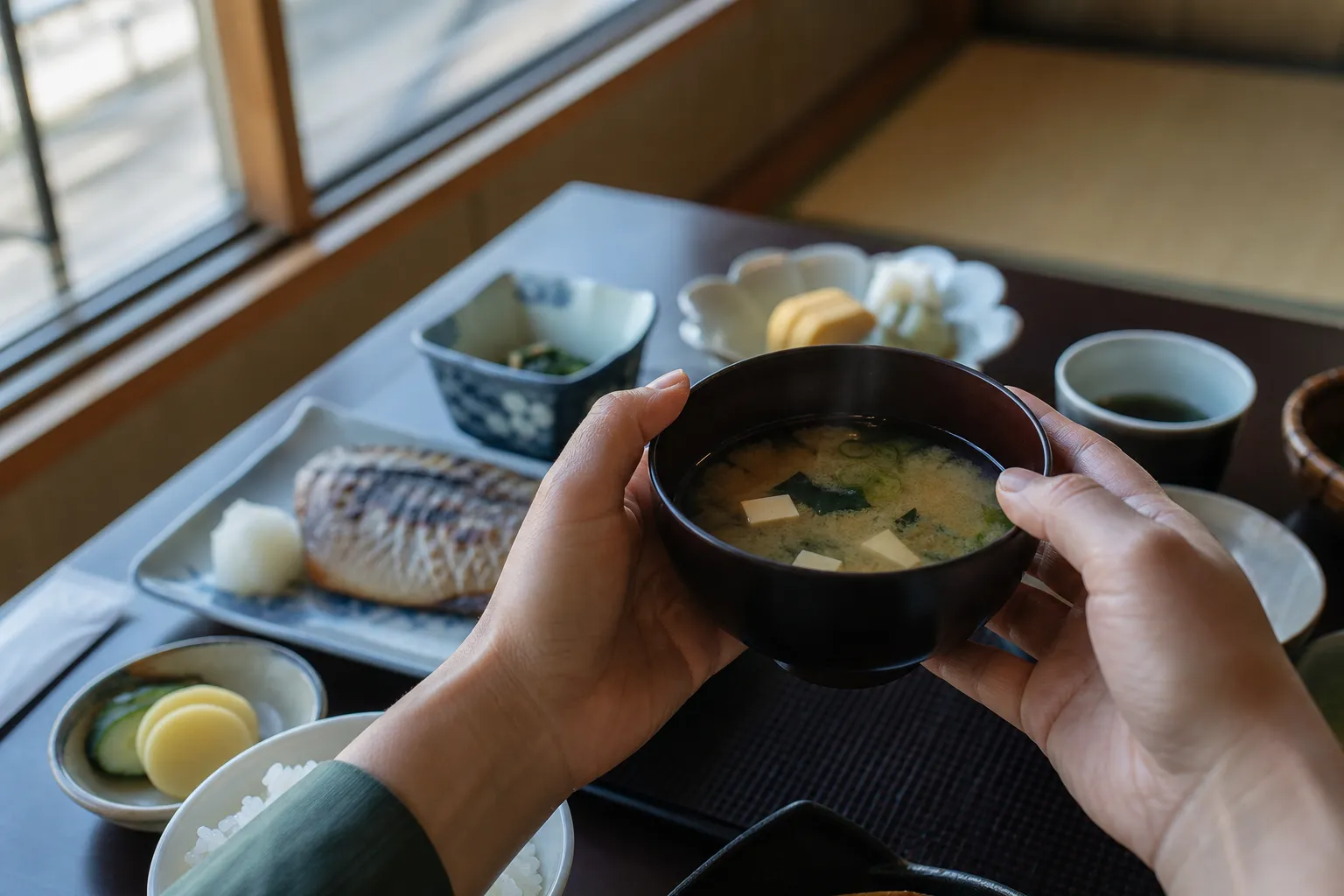 A diner lifting a lacquer bowl of miso soup during a traditional Japanese breakfast