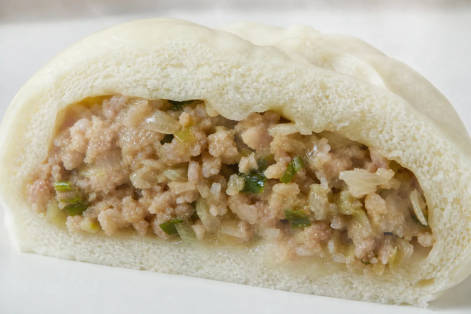 Nikuman cut open to show the savory minced pork and vegetable filling inside fluffy white steamed dough