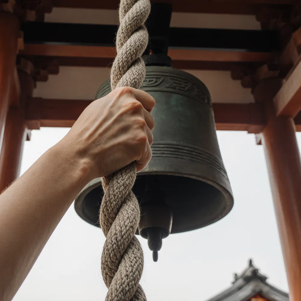 Hands ringing the shrine bell with a braided rope