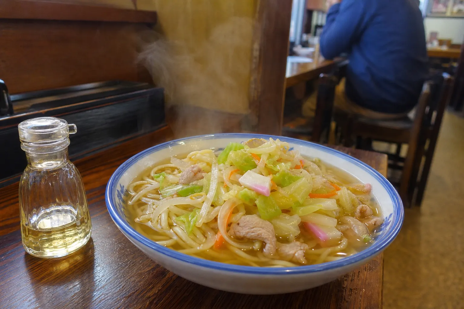 A bowl of vegetable-piled Omi champon in clear broth on a casual Shiga restaurant table with a vinegar cruet