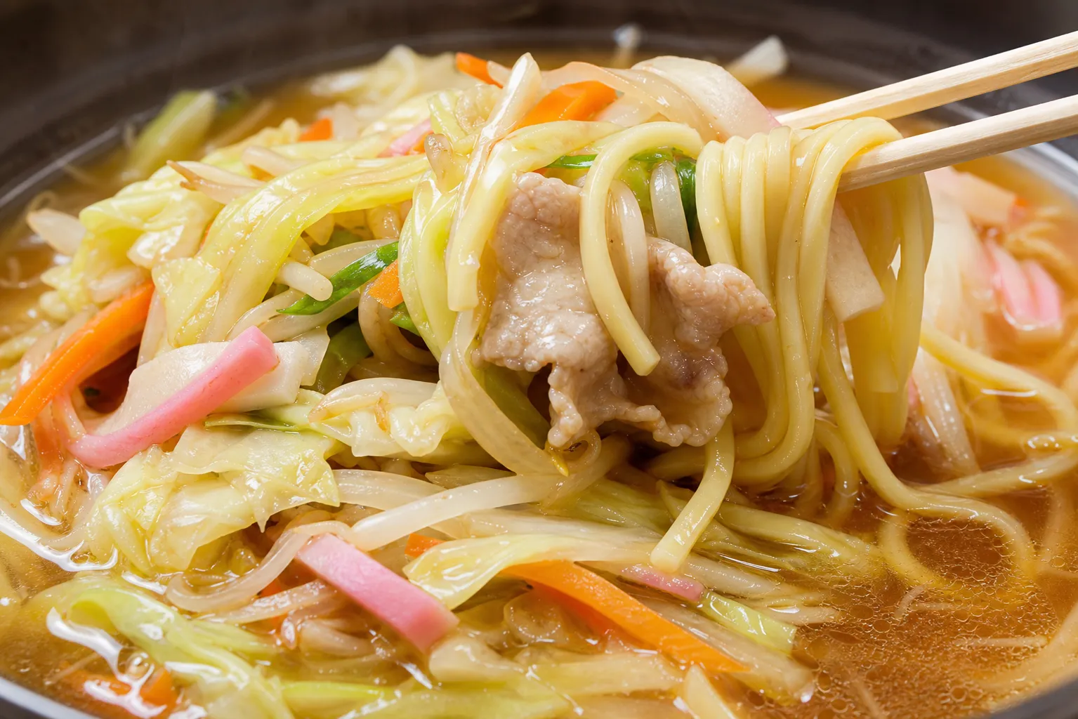 Close-up of Omi champon noodles and glistening stir-fried vegetables in a clear amber broth