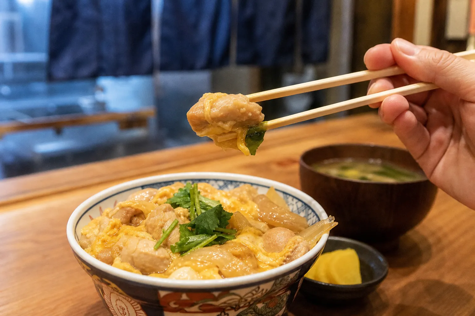 A diner lifting tender chicken from an oyakodon bowl at a neighborhood Japanese restaurant counter