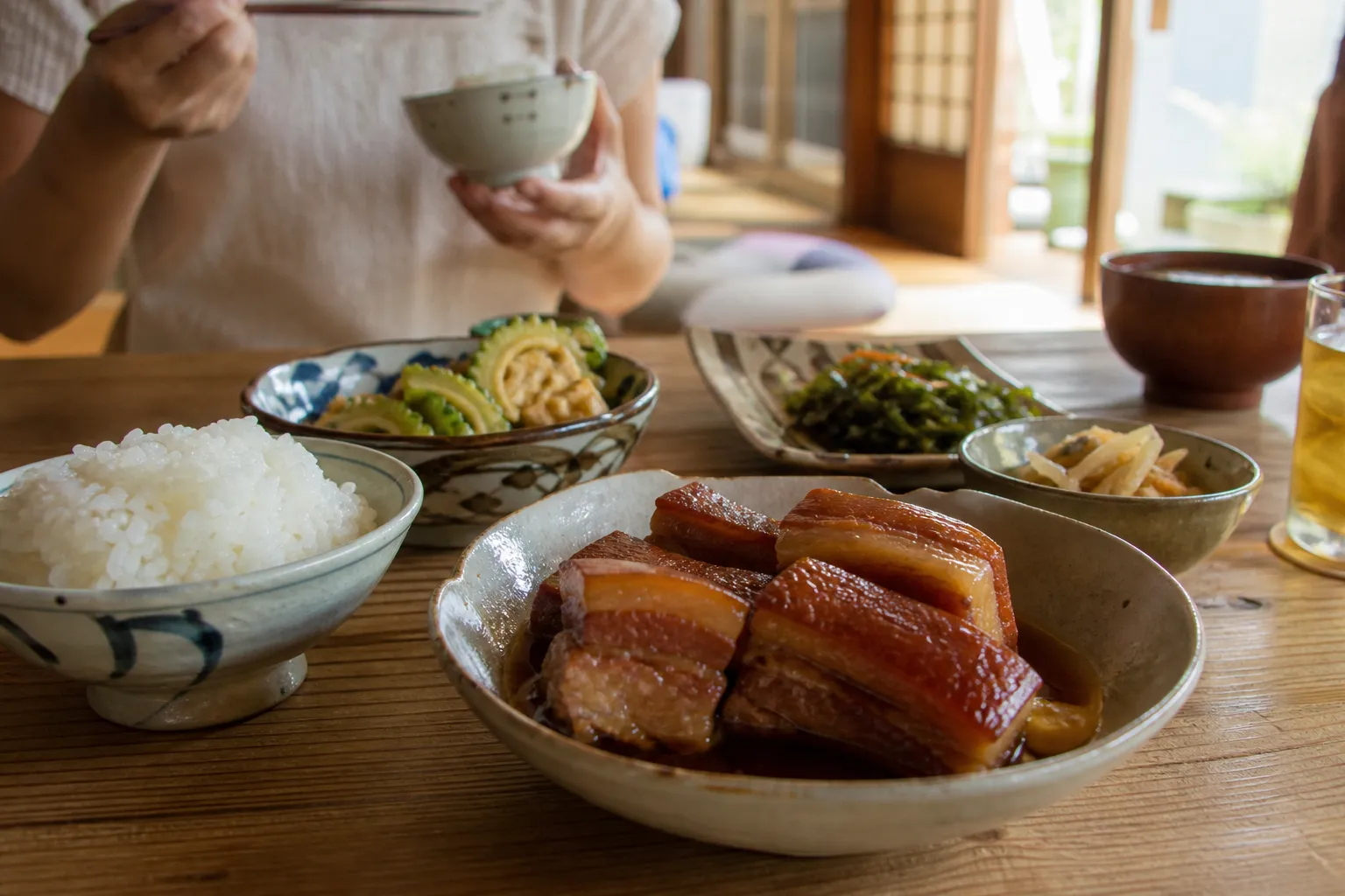 A small dish of glossy rafute pork belly as part of an Okinawan meal with rice