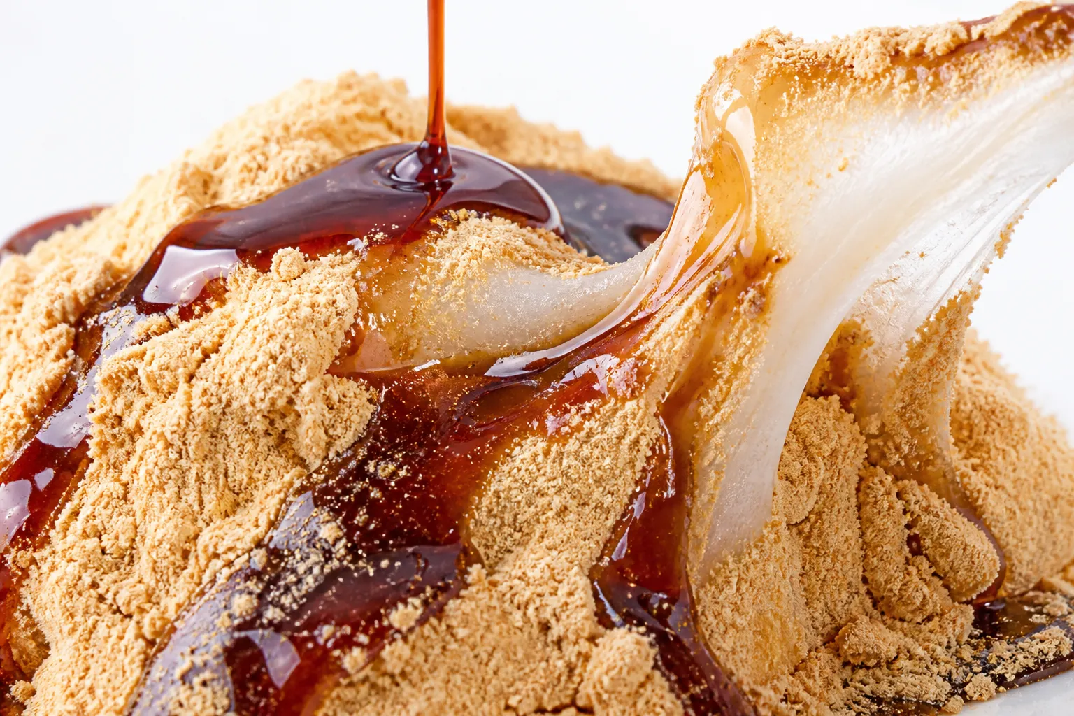 Close-up of kinako-dusted mochi with dark kuromitsu syrup pouring over it