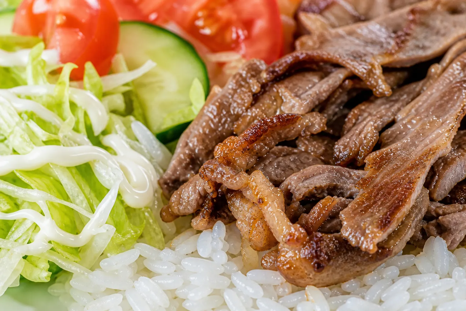 Close-up of Sicilian rice showing glossy grilled beef, fresh vegetables and mayonnaise over rice