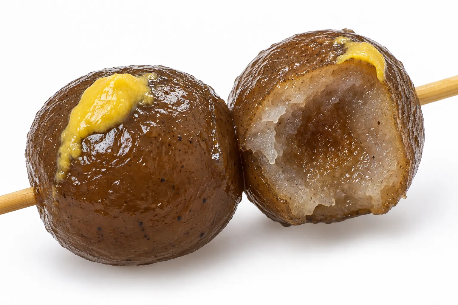 Close-up of a tama konnyaku ball bitten open showing the dense springy interior stained dark by the broth