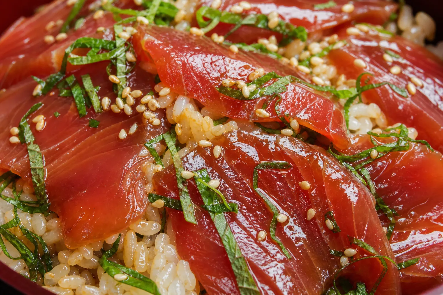 Close-up of glossy soy-marinated bonito slices over vinegared rice with shiso, ginger, sesame and nori
