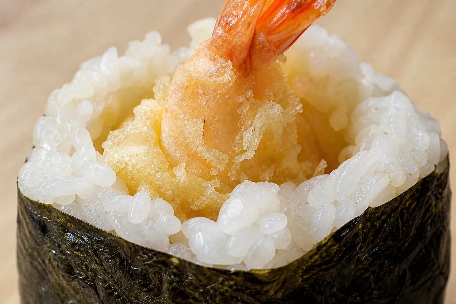 Close-up of a tenmusu bitten open to show crisp shrimp tempura inside soft salted rice and nori