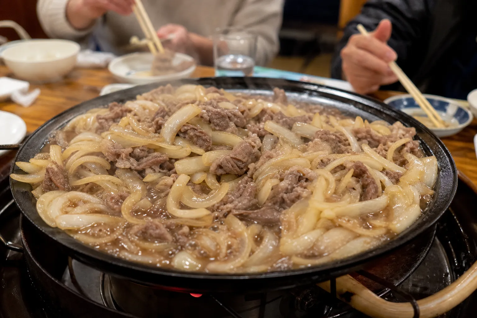 A hot plate of Towada barayaki being stir-grilled at a restaurant table, beef and onions in dark sauce