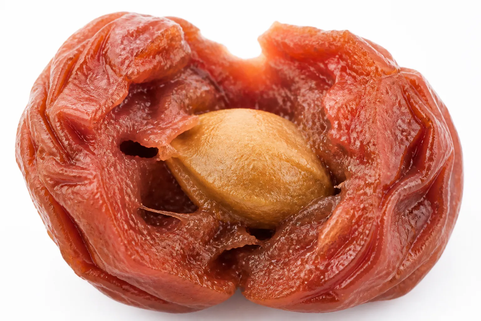 Close-up of a single umeboshi torn open showing soft red-amber flesh and the hard pit