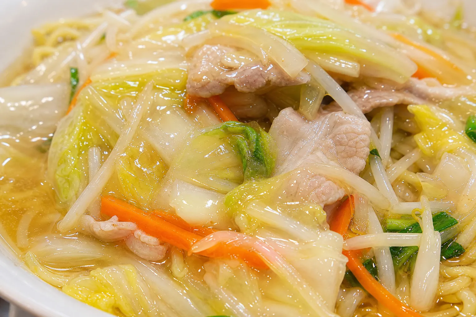 Close-up of sanma-men noodles topped with glossy stir-fried cabbage, bean sprouts, carrot and pork in a light sauce